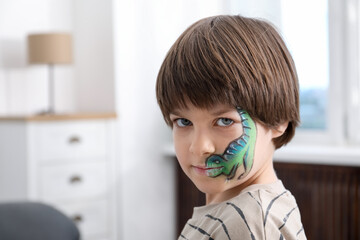 Cute boy with dinosaur face painting indoors, space for text