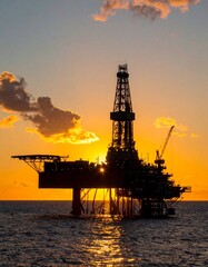 Obraz premium Silhouette of oil rig platform at sunset with small ship container nearby. 