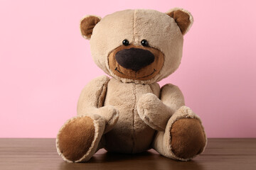 Cute teddy bear on wooden table against pink background
