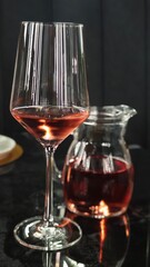 Elegant glass of rosé wine beside a pitcher on a dark background  