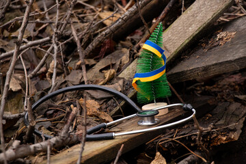 Stethoscope and Christmas tree with Ukrainian flag ribbon stand on boards against dry leaves in Ukraine in winter