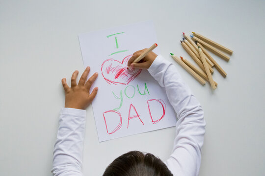 Child drawing love message for dad with colored pencils on white paper. Father day