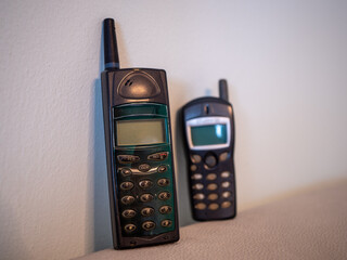 Two old mobile phones, Ericsson A1018s and Alcatel, leaning against a light wall. Classic GSM...