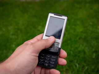 Hand holding a classic Nokia sliding mobile phone with physical keypad, photographed outdoors on...