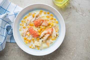 Plate of crab and corn chowder on a beige stone background, horizontal shot with space, top view