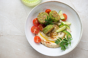 Plate with freshly made mediterranean hummus and falafel, horizontal shot on a beige stone background, top view