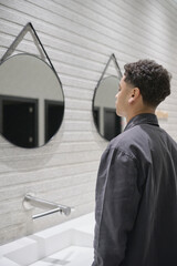 Young Dominican man fixes his taper fade haircut in front of a mirror in a public restroom at a...
