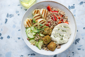 Halloumi cheese with quinoa, falafel and fresh vegetables, horizontal shot on a white and blue granite background, high angle view