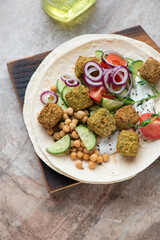 Flat bread with falafel, yogurt, fresh vegetables and chickpeas, vertical shot on a brown granite background, high angle view