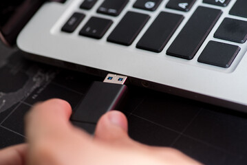 Hand inserting Flash drive memory drive plugged into a computer laptop port.