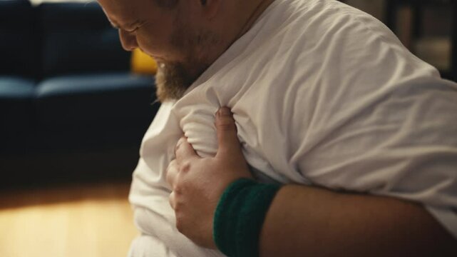Large-bodied man holding chest during home workout, heart pain, health warning