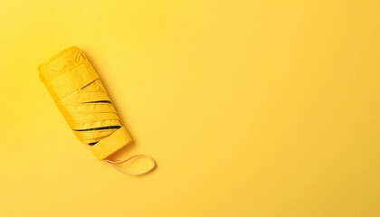 Bright yellow compact umbrella neatly folded on a yellow background for rainy day essentials
