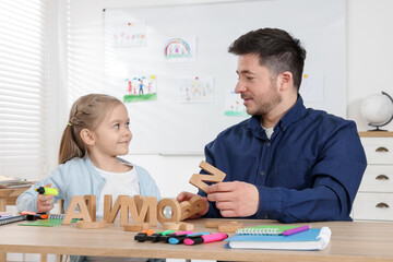Little girl learning letters with teacher at desk indoors