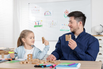Little girl learning letters with teacher at desk indoors