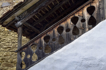 Old wooden carved railings of outdoor staircase against background of ancient wall with stonework....