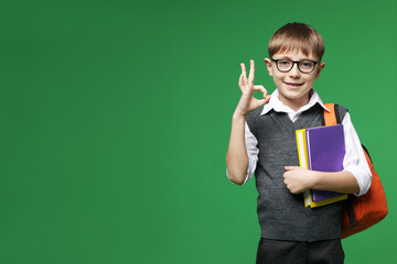 Cute schoolboy with backpack and books showing ok gesture on green background, space for text