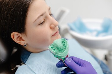 Dentist showing dental mold to young patient in clinic