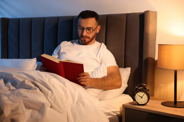 Young man reading book in bed at home