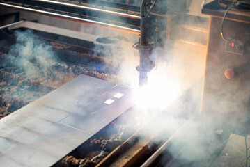 Plasma cutting process in metal fabrication workshop with smoke and sparks during operation