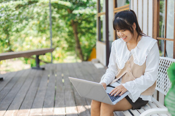 Asian woman is happily working on her laptop outdoors enjoying remote digital nomad lifestyle in...