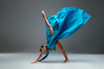 Dancer in sport leotard doing Split. Cheerleader dancing with flying blue cloth fabric. Graceful ballerina dancing on grey studio background. Child, artist, movement, action and motion concept