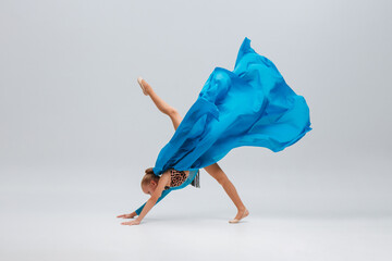 Dancer in sport leotard doing Split. Cheerleader dancing with flying blue cloth fabric. Graceful ballerina dancing on grey studio background. Child, artist, movement, action and motion concept