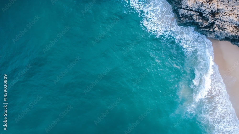 Poster aerial view of turquoise ocean waves breaking on a sandy beach next to rocky cliffs, creating a stun