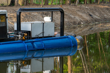 Dredge positioned on waterway, conveying material with engine and pipes, with vegetation reflected in water.