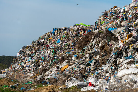 Overfilled landfill with huge mountain of mixed waste against a light blue sky on a sunny day suggesting environmental damage