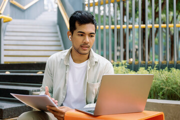 Young asian freelancer working remotely with laptop and documents outdoors