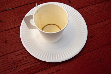 A white paper coffee cup with a handle placed on a white paper plate set on a rustic red wooden table in an outdoor cafe in Hamina, Finland