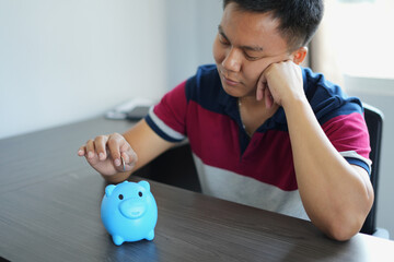 Sad and depressed caucasian business man laying on the table with a piggy bank and counting his...