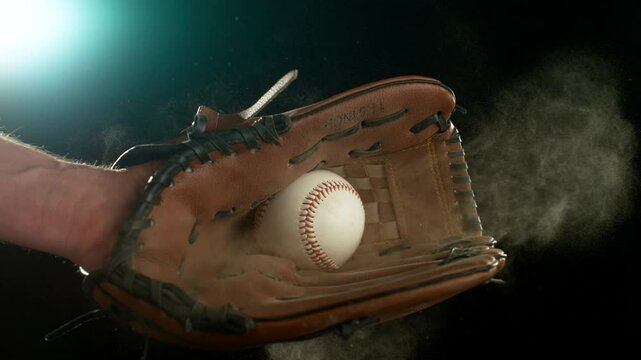 Super slow motion of hand in brown leather baseball glove caught ball isolated on black background . Filmed on high speed cinematic camera