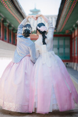 Fototapeta premium Rear view of two young women wearing traditional Korean hanbok making a heart shape with their hands at the historic Gyeongbokgung Palace in Seoul, South Korea.