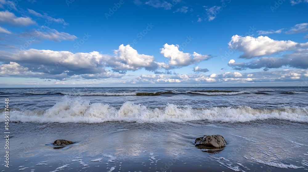 Aufkleber ocean waves rolling onto a sandy beach under a partly cloudy blue sky, two rocks partially submerged
