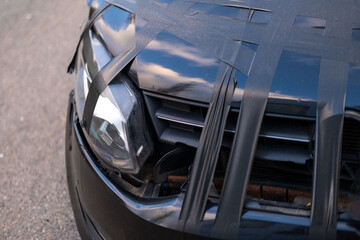 damaged black car after crash, hood taped with duct tape, scratched surface, Urban accident detail,...