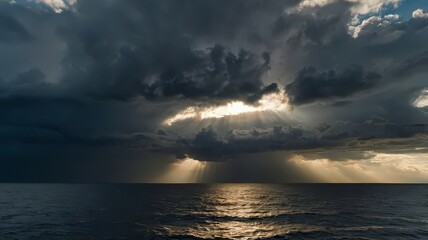 Obraz premium Sun rays pierce through dark storm clouds over the ocean creating a dramatic and moody atmosphere