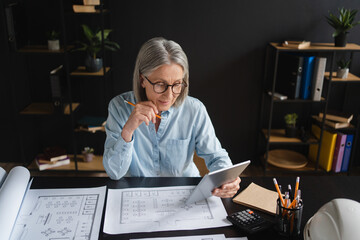 Mature woman, architect and reading with tablet, screen and ideas with review, floor plan or...