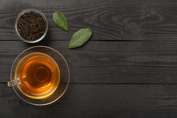 Cup of tea with dry and fresh leaves on wooden background, top view