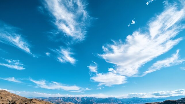 Serene landscape featuring a vibrant blue sky adorned with wispy cirrus clouds, overlooking a majestic mountain range on a clear, sunny day. : Generative AI - Powered by Adobe