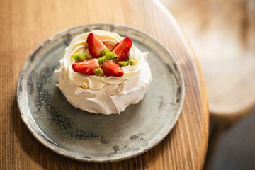 Pavlova cake with whipped mascarpone cream and fresh strawberry slices in cafe.