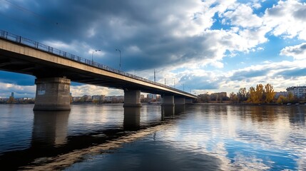 A long concrete bridge stretches across a wide river, its reflection mirrored in the calm water under a partly cloudy sky.  Buildings and autumnal trees line the riverbanks. : Generative AI