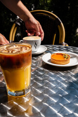 Sipping on a chilled drink while relishing a creamy dessert at a sunlit outdoor table