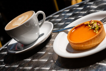 Enjoying a rich, sweet tart topped with nuts alongside a frothy coffee on a sunny day