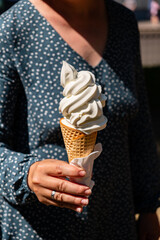 A person joyfully holds a cone of soft serve ice cream, savoring a sunny day outdoors