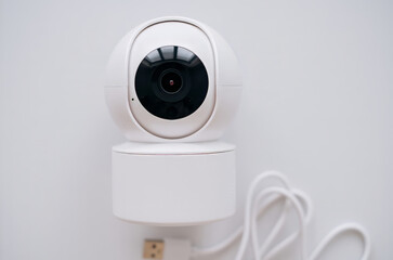 Close-up image of a modern white smart security camera mounted on a wall with a USB cable attached