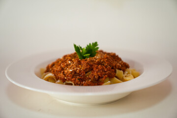 Top view of fettuccine pasta with tomato sauce, cheese and parsley on a white plate isolated on white background.