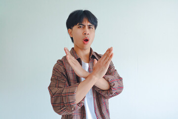 Serious young Asian man making a stop gesture with hand, isolated on white background, showing...