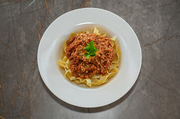 Top view of fettuccine pasta with tomato sauce, cheese and parsley on a white plate on a table.
