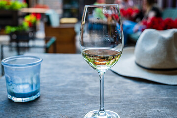 A glimmering glass of white wine rests on a rustic table, capturing sunlight amidst joyful chatter